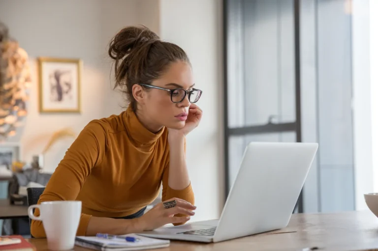 Woman working on her laptop from home with a cup of coffee and notepad on the table